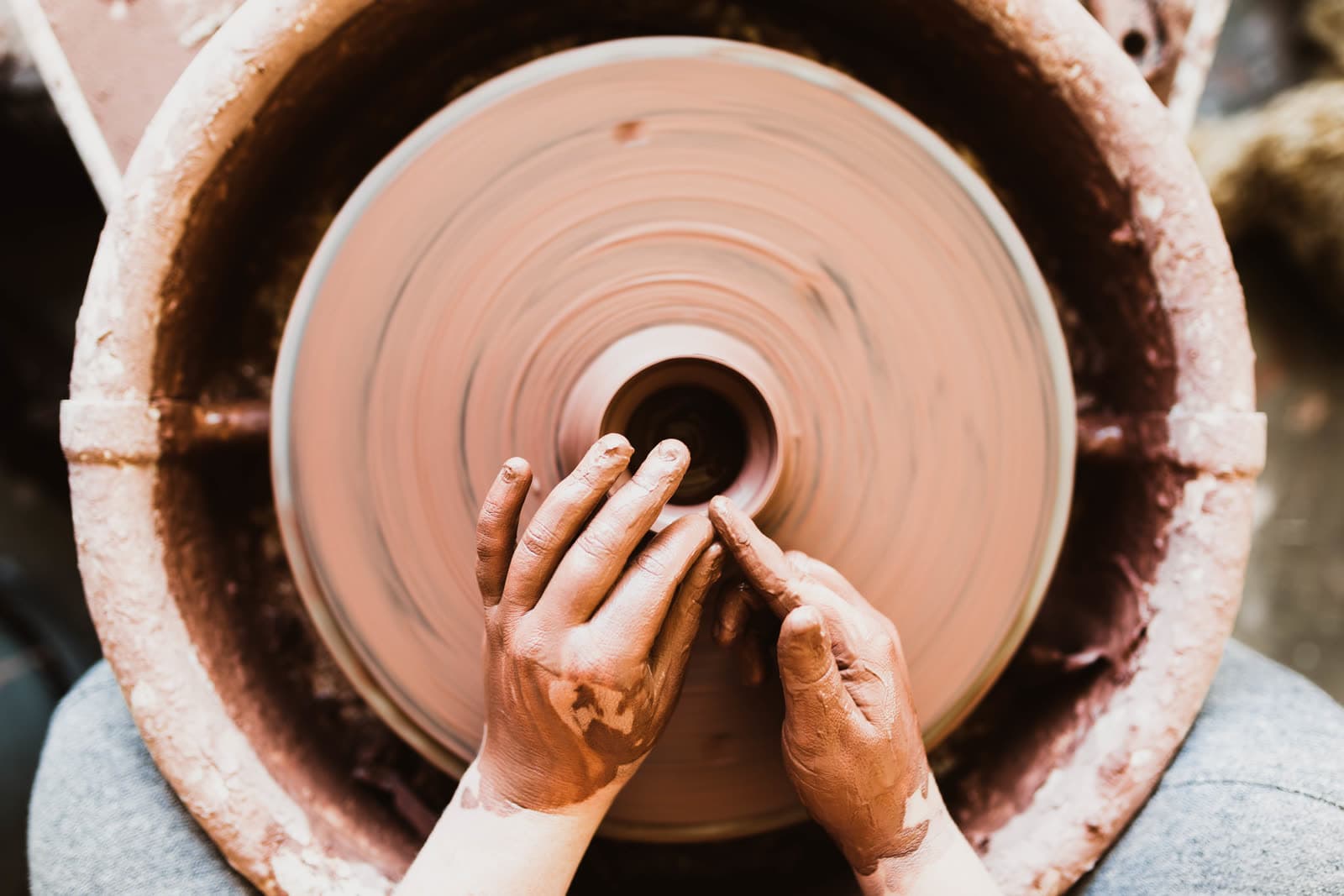 Clay-covered hands shaping a pot on a wheel